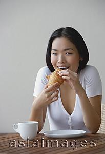 Asia Images Group - Young woman eating a croissant