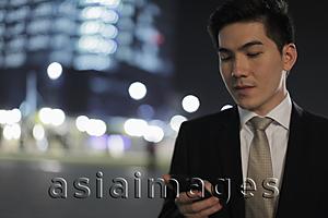 Asia Images Group - Young man texting on phone at night, buildings in background