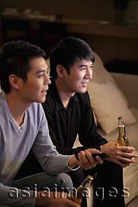Asia Images Group - Young men watching TV and holding bottles of beer