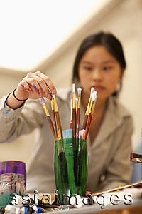 Asia Images Group - Young woman, out of focus, choosing paintbrushes in an art studio