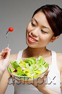AsiaPix - Woman looking at tomato on fork and holding bowl of salad