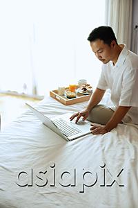 AsiaPix - Man sitting on bed, using laptop