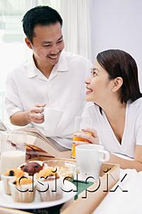 AsiaPix - Couple on bed, with drinks, looking at each other, breakfast tray in front of them