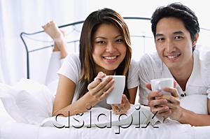 AsiaPix - Couple on bed, holding mugs, smiling at camera, portrait
