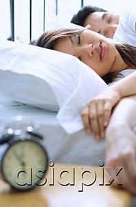 AsiaPix - Couple sleeping on bed, alarm clock in foreground, selective focus