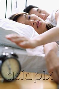 AsiaPix - Couple lying on bed, woman reaching to switch of alarm clock in foreground