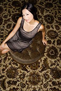 AsiaPix - Woman sitting on oriental carpet, looking at camera
