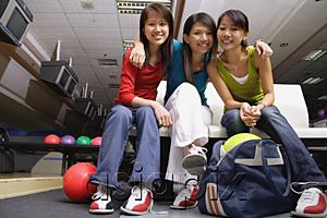 AsiaPix - Women sitting side by side in bowling alley, smiling at camera