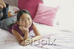 AsiaPix - Girl lying on bed, hands on chin, smiling at camera