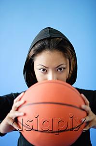 AsiaPix - Woman wearing hooded shirt, holding basketball over face