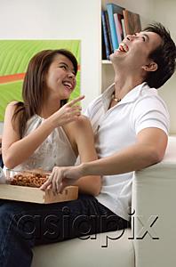 AsiaPix - Couple at home in living room, sitting on sofa, laughing