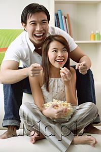 AsiaPix - Couple at home in living room, watching TV, eating popcorn