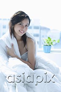 AsiaPix - Young woman sitting on bed, wrapped in a blanket, smiling at camera
