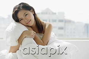 AsiaPix - Young woman sitting on bed, embracing pillow
