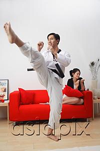 AsiaPix - Couple at home, man practicing martial arts, woman sitting on sofa, filing her nails