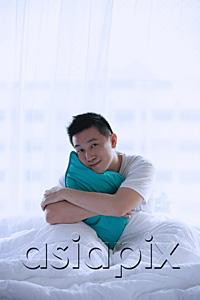 AsiaPix - Man sitting in bed, embracing pillow, smiling at camera