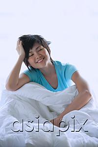 AsiaPix - Woman sitting on bed, smiling, eyes closed