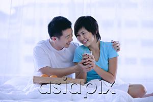AsiaPix - Couple sitting on bed, having breakfast, woman holding glass of milk