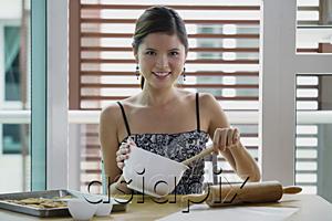 AsiaPix - Young woman in kitchen holding mixing bowl, smiling at camera