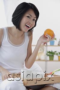 AsiaPix - Young woman having breakfast in bed, holding orange, smiling