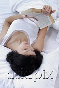 AsiaPix - Young woman lying on bed, reading a book, high angle view
