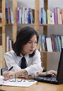 AsiaPix - Young woman in library, using laptop and writing