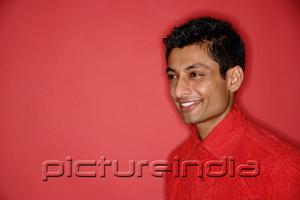 PictureIndia - Man in red shirt against red background, looking away