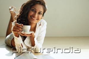 PictureIndia - Woman lying on front, holding cup and saucer, smiling