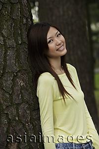 Asia Images Group - Young woman leaning against tree and smiling