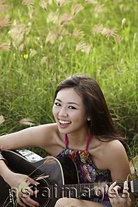 Asia Images Group - smiling woman playing guitar on grass