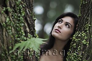 Asia Images Group - Head shot of young woman looking up with tree in foreground