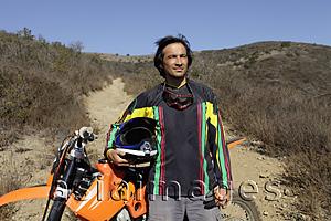 Asia Images Group - Man standing in front of motorcycle in front of dirt road