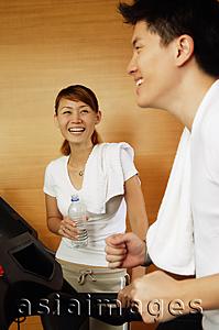 Asia Images Group - Couple in gym, man on treadmill, woman holding bottle of water