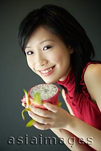 Asia Images Group - Woman holding cut dragon fruit, smiling at camera