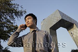 Asia Images Group - Young man speaking on phone in front of the CCTV Building