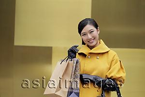 Asia Images Group - Young woman in  yellow coat holding shopping bags