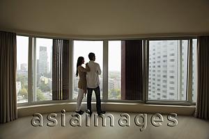 Asia Images Group - Rear view of young couple looking out large windows of condo