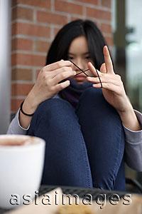 Asia Images Group - Young woman sitting at a cafe, playing with string