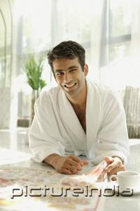 PictureIndia - Man in bathrobe, lying on floor, with newspaper, smiling at camera
